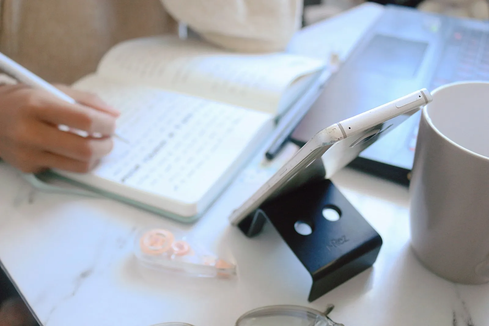 Hand writing notes beside a laptop and phone